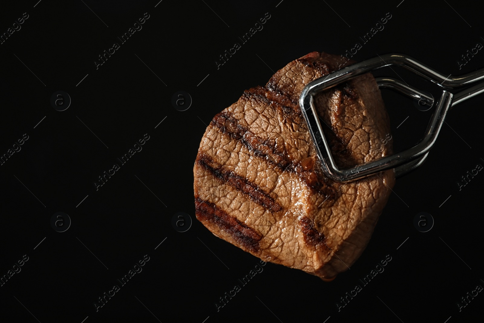 Photo of Food tongs with grilled steak and space for text on black background. Tasty meat