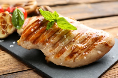 Tasty grilled chicken fillet with green basil on wooden table, closeup
