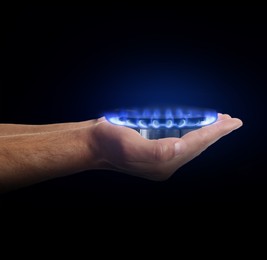 Closeup view of man holding gas burner with blue flame on black background
