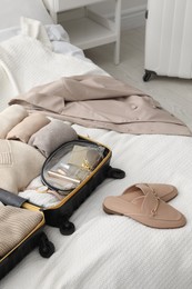 Photo of Open suitcase with folded clothes, shoes and accessories on bed in room