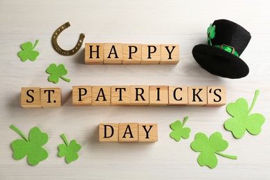 Photo of Wooden cubes with words Happy St Patrick's Day, leprechaun hat and decorative clover leaves on white table, flat lay