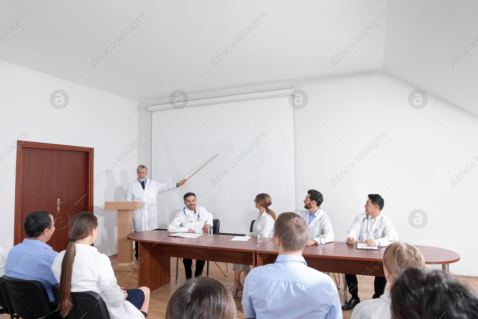 Photo of Senior doctor giving lecture in conference room with projection screen