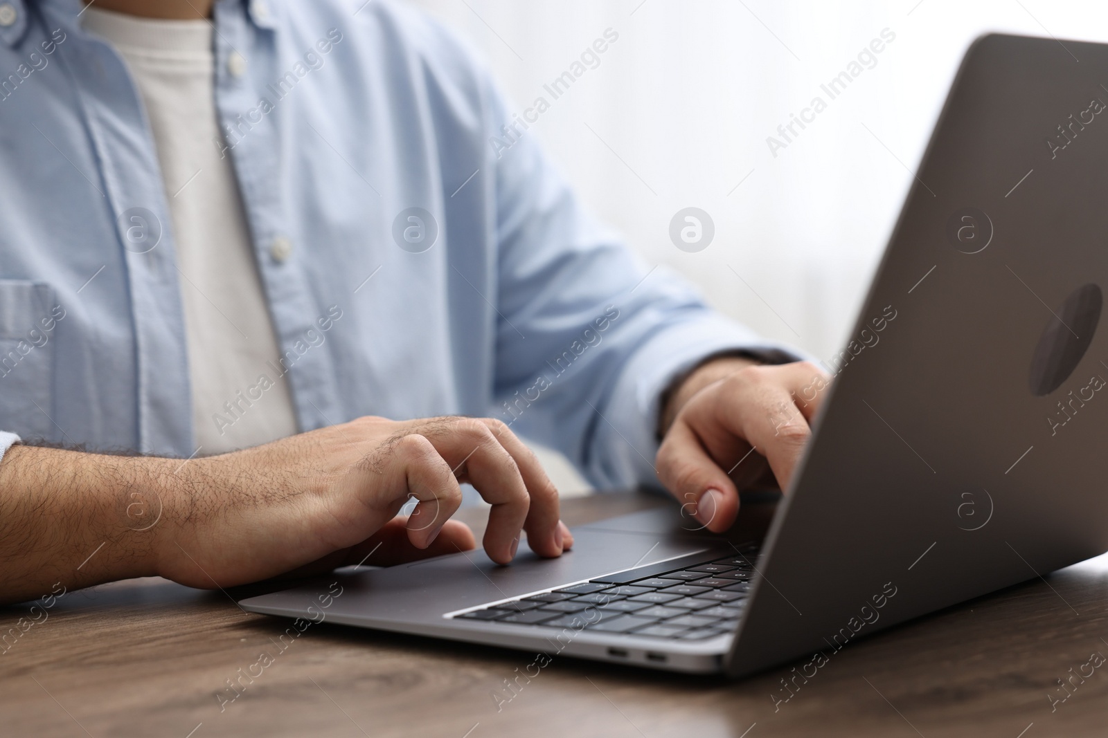 Photo of E-learning. Young man using laptop at wooden table, closeup