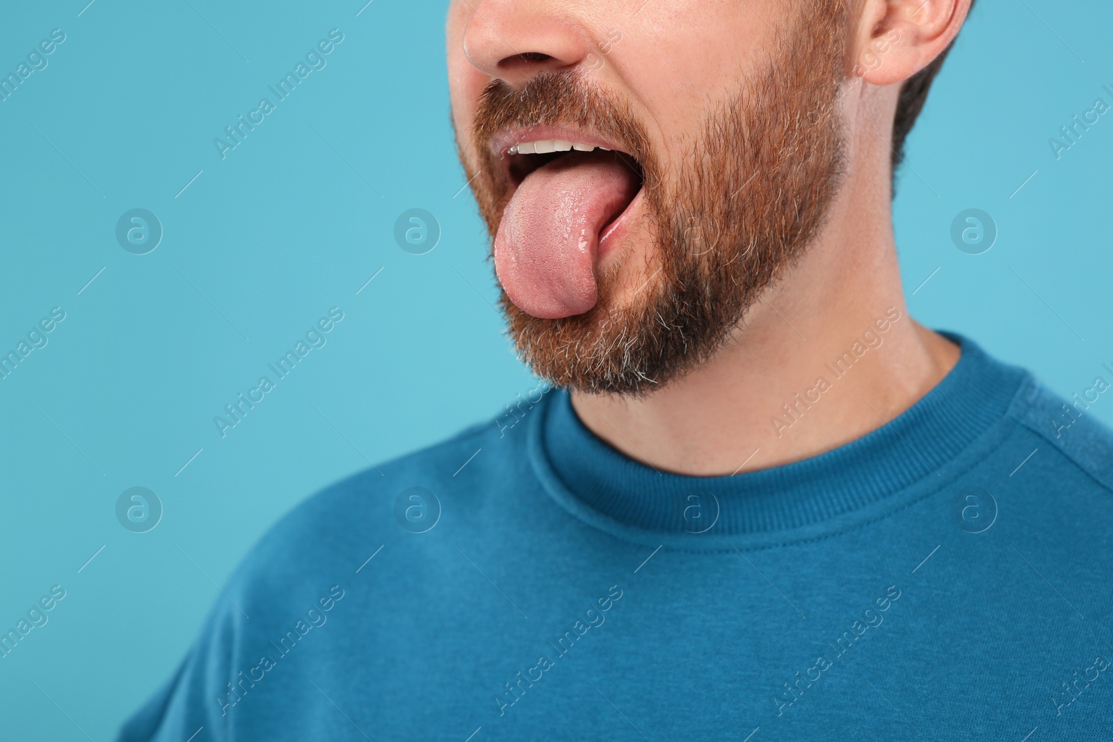 Photo of Man showing his tongue on light blue background, closeup