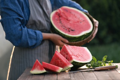 Photo of Woman holding wicker basket outdoors, closeup. Focus on delicious ripe watermelon slices with mint