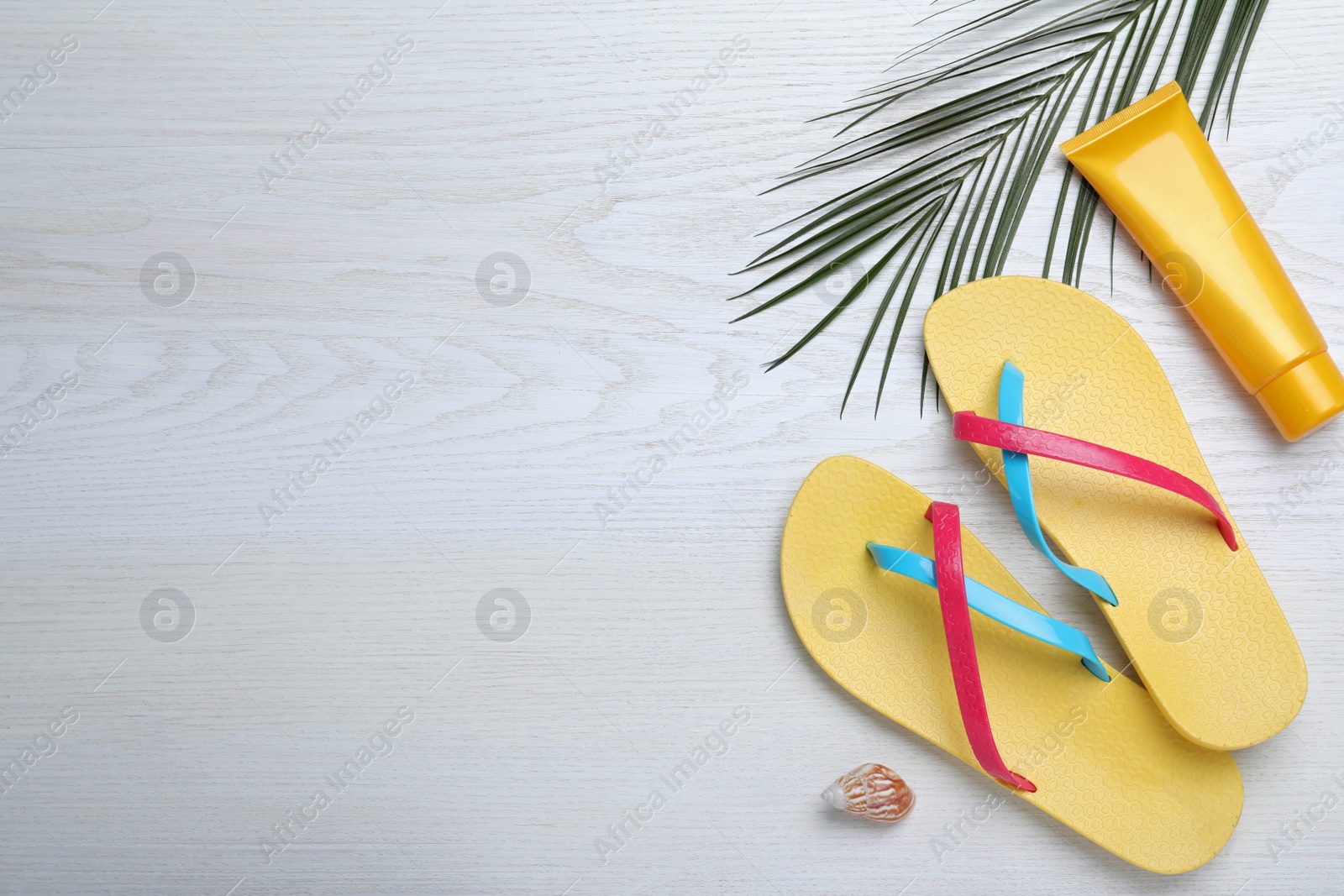 Photo of Stylish flip flops and sun protection product on white wooden background, flat lay. Space for text