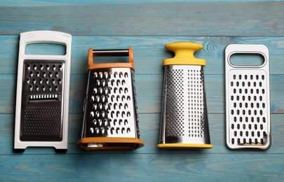 Photo of Different modern graters on light blue wooden table, flat lay