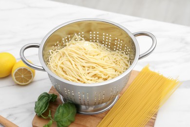 Photo of Cooked pasta in metal colander and products on white marble table, closeup