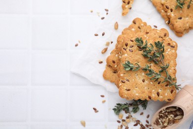 Cereal crackers with flax, sesame seeds and thyme on white tiled table, flat lay. Space for text