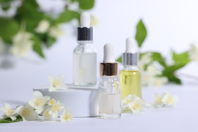 Photo of Presentation of essential oils in bottles and beautiful jasmine flowers on white background, closeup