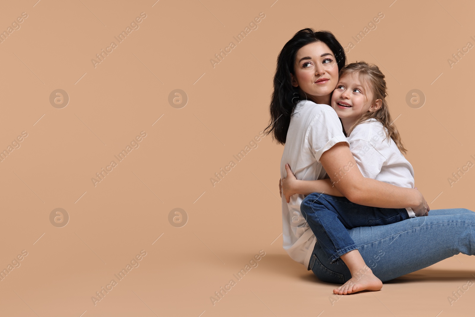 Photo of Beautiful mother with little daughter sitting on beige background. Space for text