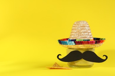 Delicious guacamole, nachos chip, Mexican sombrero hat and fake mustache on yellow background. Space for text