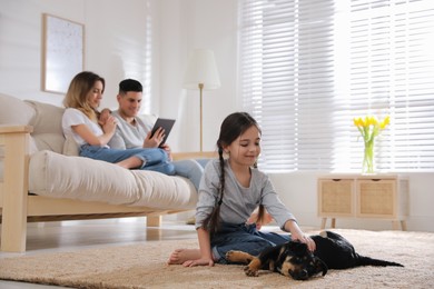 Photo of Little girl playing with puppy while parents sitting on sofa in living room