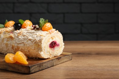 Photo of Tasty meringue roll with jam, tangerine slices and mint leaves on wooden table, closeup. Space for text