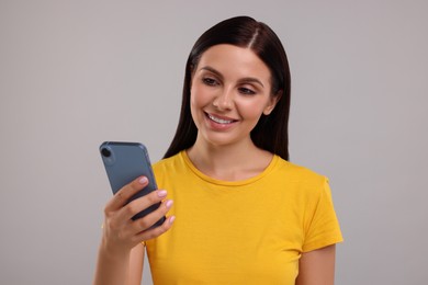 Photo of Young woman using smartphone on grey background