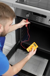 Professional serviceman repairing modern oven in kitchen