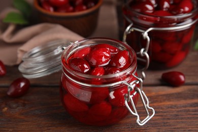 Photo of Delicious dogwood jam with berries in glass jar on wooden table, closeup