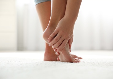 Photo of Young woman suffering from pain in foot indoors, closeup