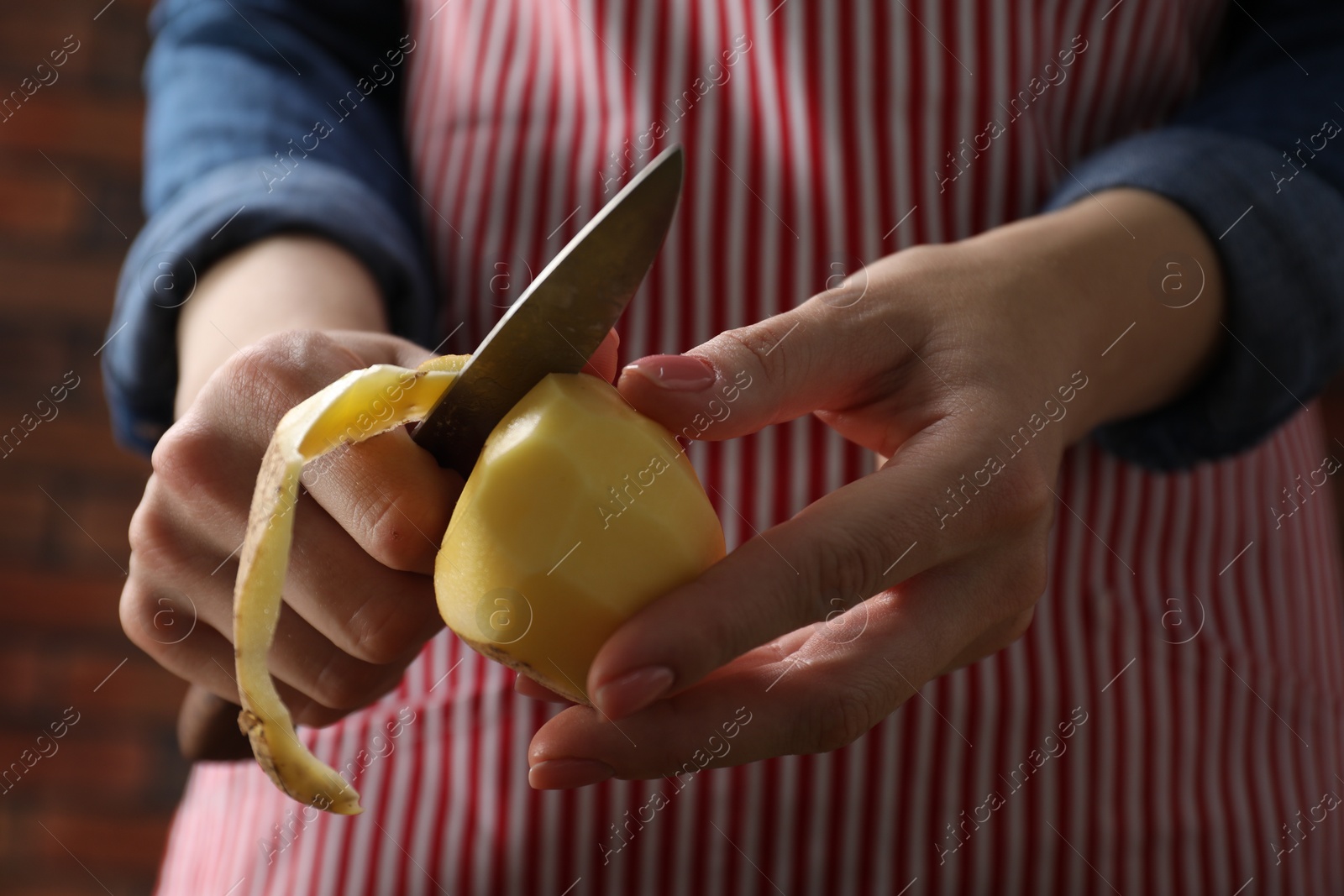 Photo of Woman peeling fresh potato with knife indoors, closeup