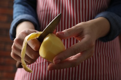 Photo of Woman peeling fresh potato with knife indoors, closeup