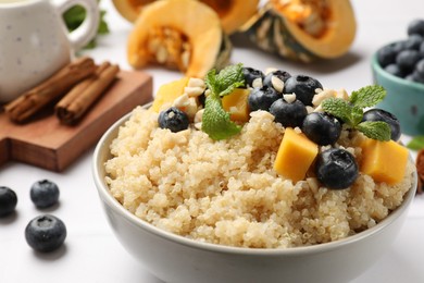 Photo of Tasty quinoa porridge with blueberries, pumpkin and mint in bowl on white table, closeup