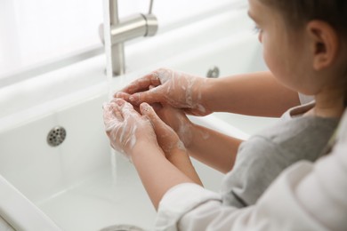 Photo of Mother and daughter washing hands with liquid soap together at home, closeup
