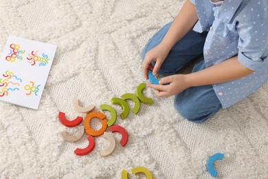 Photo of Motor skills development. Girl playing with colorful wooden arcs on carpet, above view