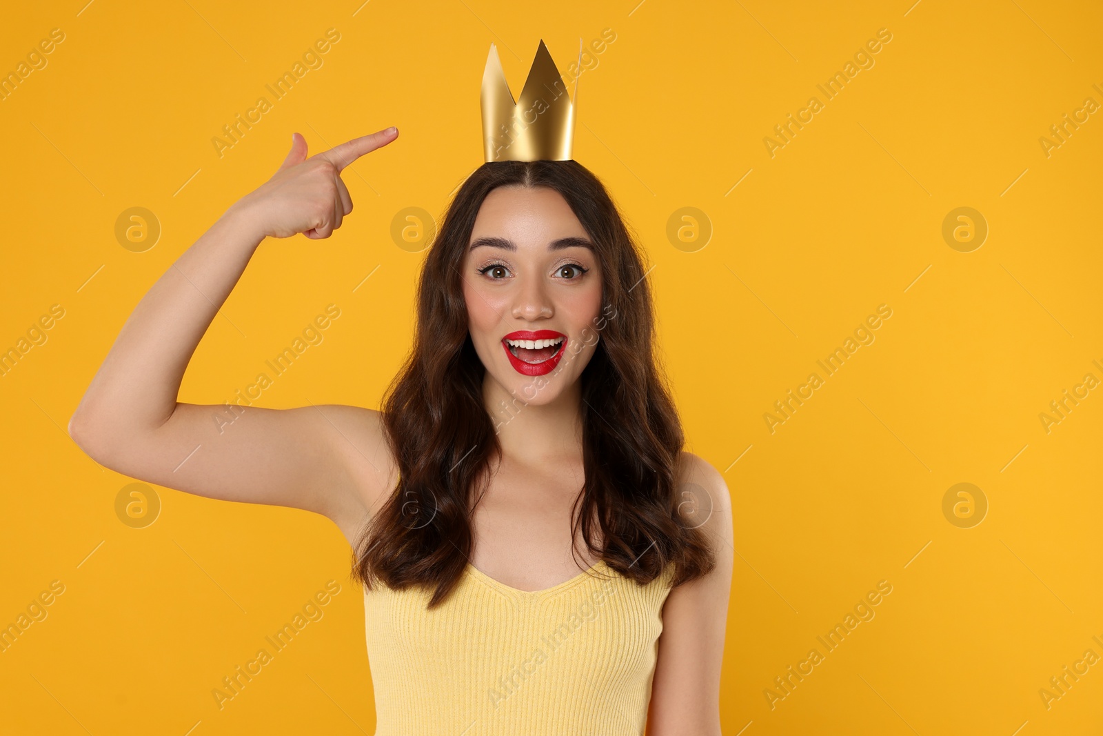 Photo of Beautiful young woman pointing at princess crown on yellow background