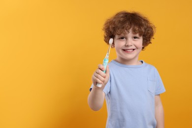 Photo of Cute little boy holding electric toothbrush on yellow background. Space for text