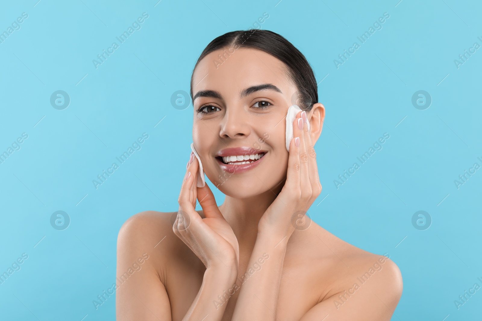 Photo of Beautiful woman removing makeup with cotton pads on light blue background