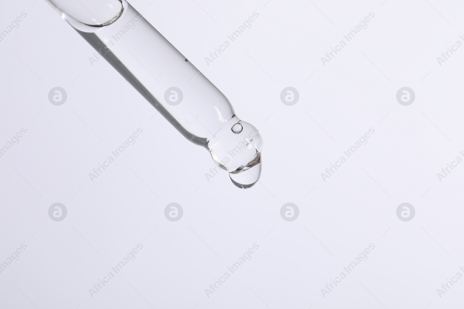 Photo of Dripping cosmetic serum from pipette on white background, space for text