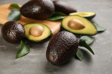 Whole and cut avocados with green leaves on grey table, closeup