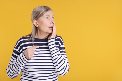 Portrait of surprised senior woman on yellow background, space for text