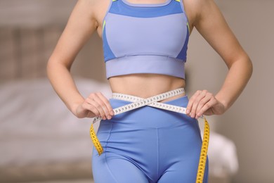 Woman in sportswear measuring waist with tape at home, closeup