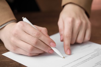 Woman signing documents at wooden table in office, closeup
