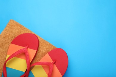 Photo of Flip flops and towel on light blue background, top view. Space for text