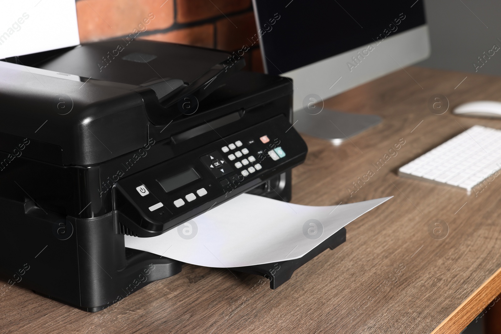 Photo of Modern printer with paper near computer on wooden desk at home