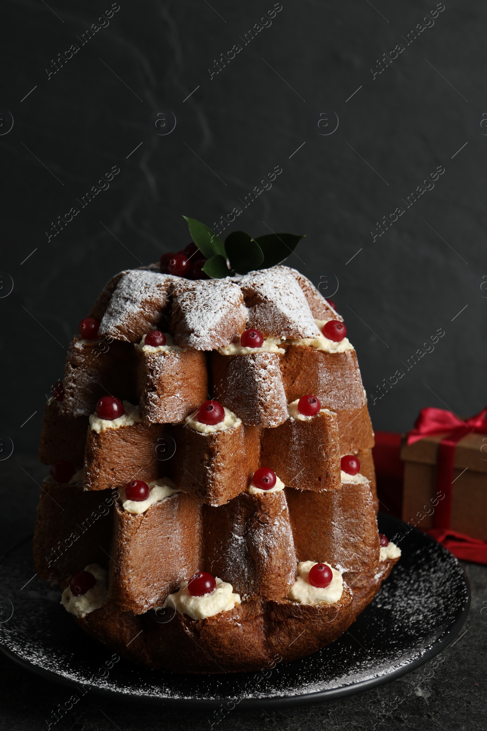 Photo of Delicious Pandoro Christmas tree cake with powdered sugar and berries near festive decor on black table