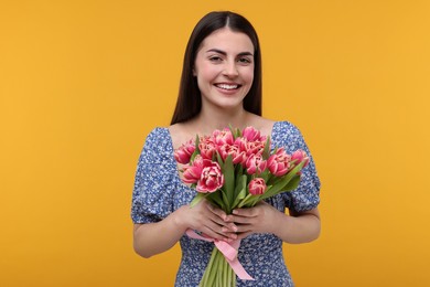 Happy young woman with beautiful bouquet on orange background