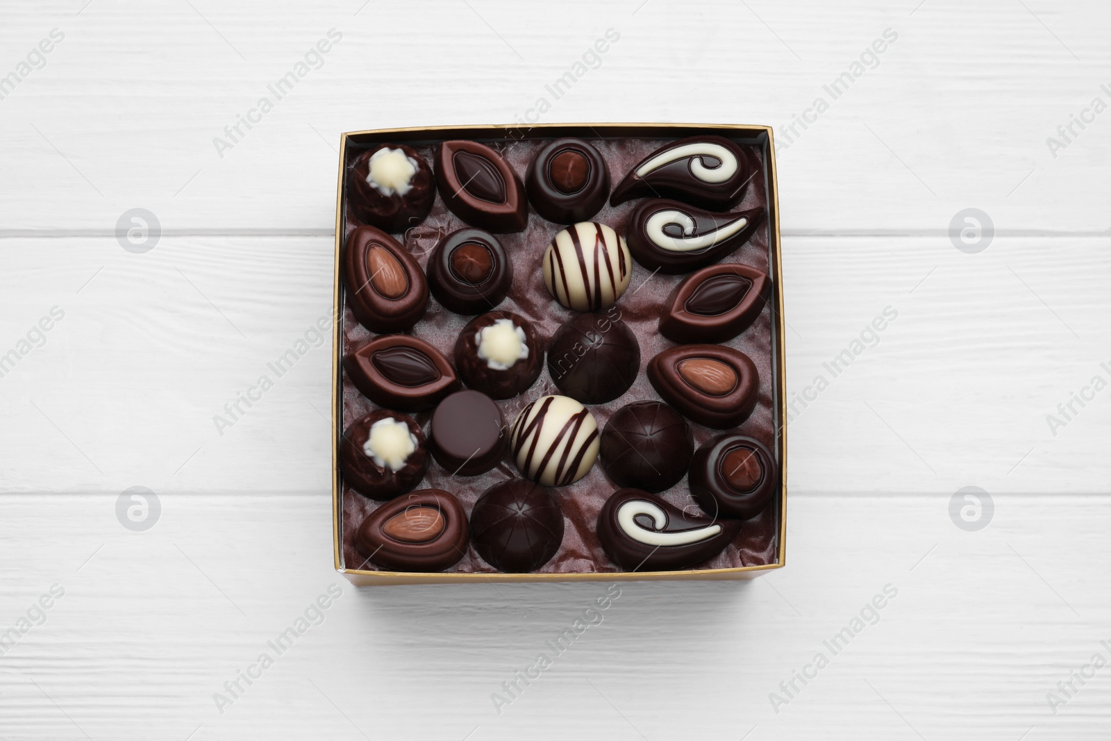 Photo of Box of delicious chocolate candies on white wooden table, top view