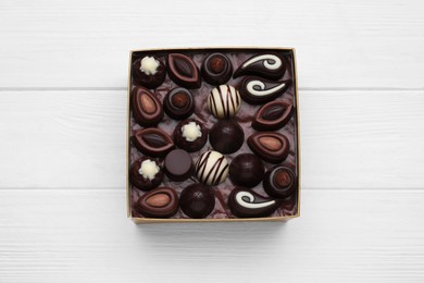 Box of delicious chocolate candies on white wooden table, top view