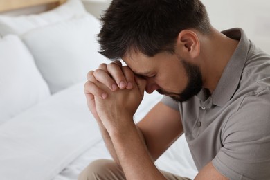 Religious man with clasped hands praying in bedroom