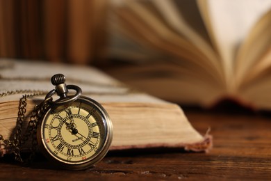 Photo of Pocket clock with chain and book on wooden table, closeup. Space for text