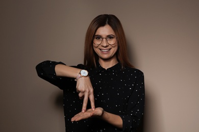 Woman showing STAND gesture in sign language on color background