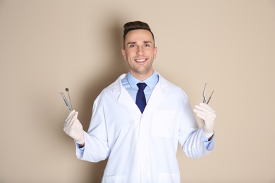 Photo of Male dentist holding professional tools on color background