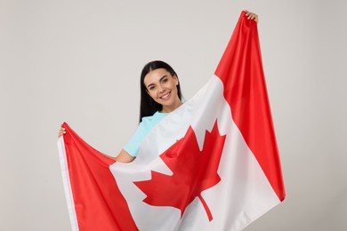 Happy young woman with flag of Canada on beige background