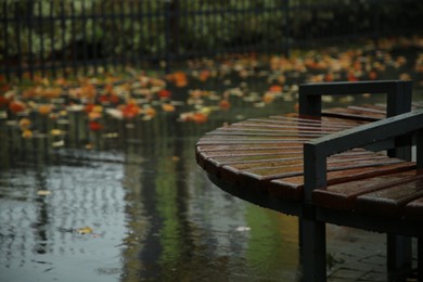 Photo of Wet wooden bench on city street after rain, space for text
