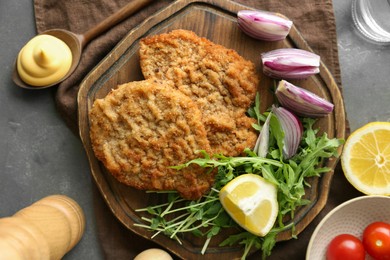 Delicious schnitzels served with lemon, onion and microgreens on grey table, flat lay