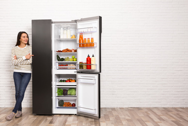 Photo of Happy young woman near open refrigerator indoors, space for text