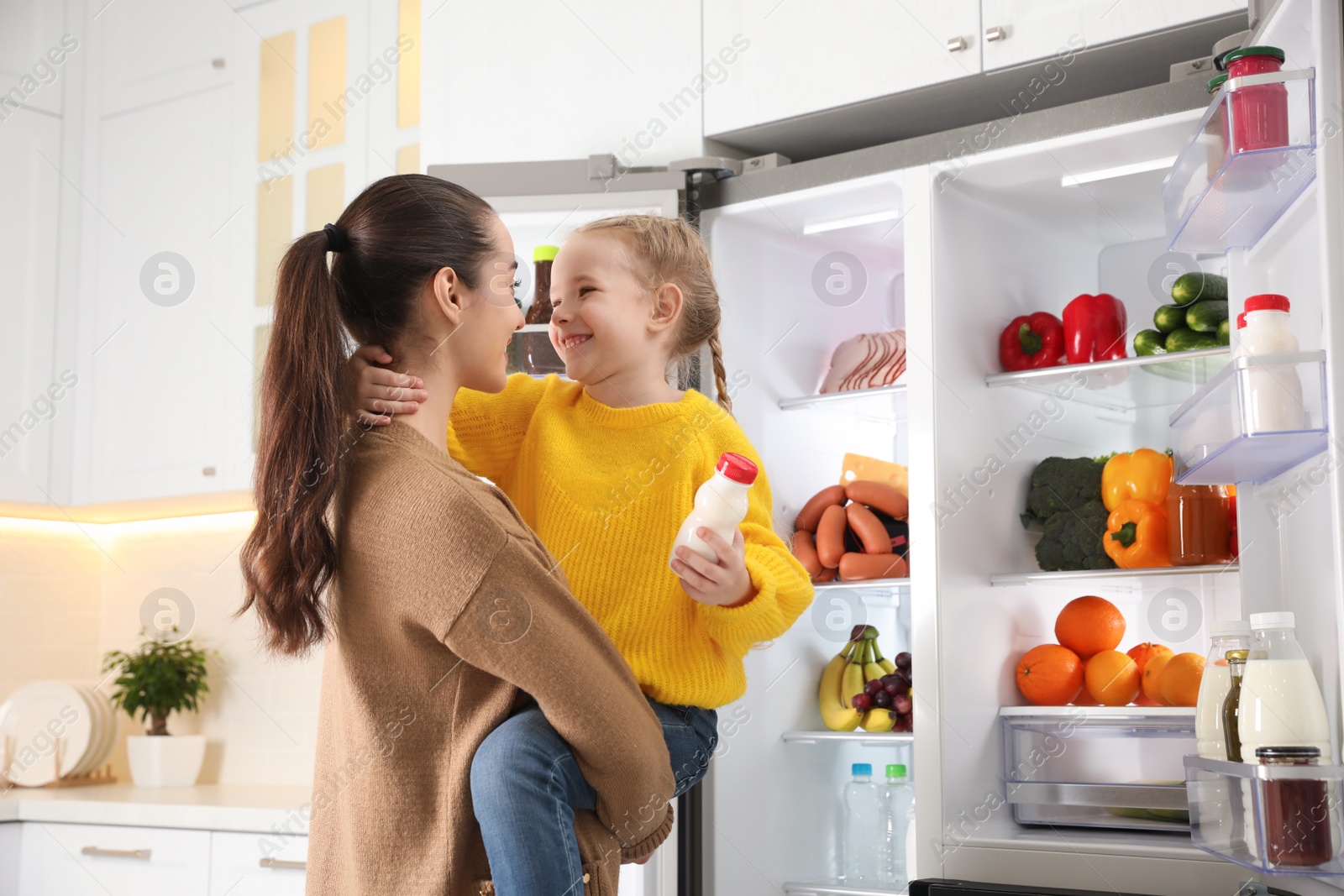 Photo of Young mother and daughter near open refrigerator in kitchen